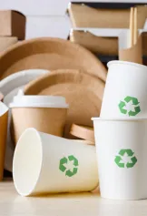 Assorted paper packaging goods, such as plates, cups, and containers, with green recycling symbols